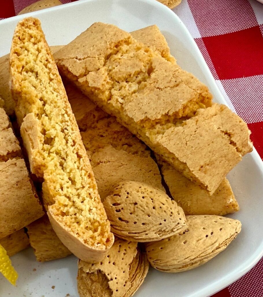 Amaretto Biscottini in a white square deep dish on a red checkered tablecloth, surrounded by whole almonds in their shells.
