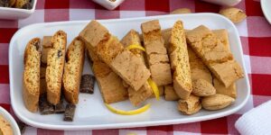 Chocolate, Lemon, and Amaretto Biscottini served on a white plate with a cup of coffee on a red checkered tablecloth.
