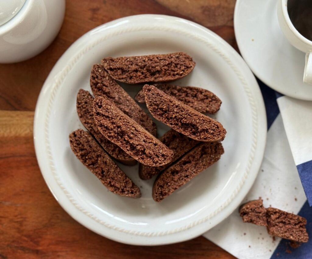 Round white plate stacked with Chocolate Anise Biscottini beside a cup of tea.