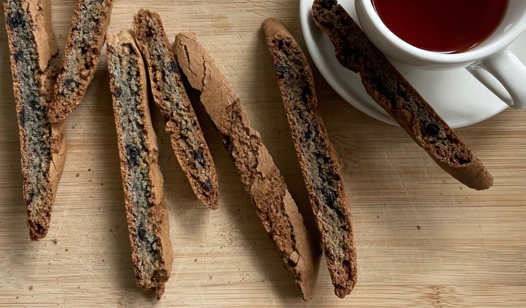 A rustic wooden board with fruit biscotti and a cup of tea in the top right corner
