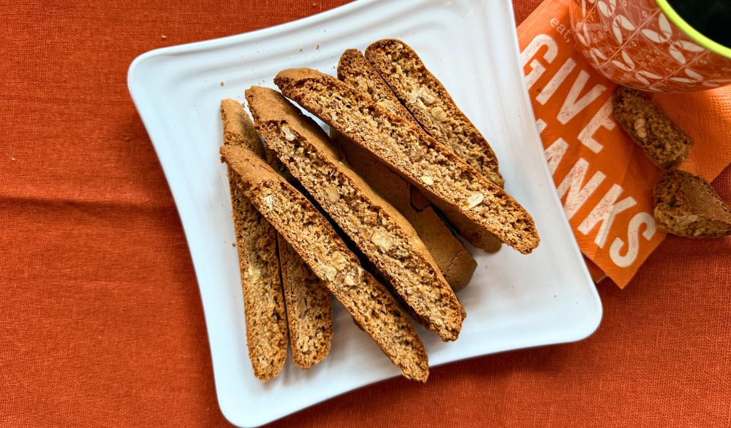 Gluten free pumpkin spice biscotti next to a hot cup of coffee and a napkin that says Give Thanks.