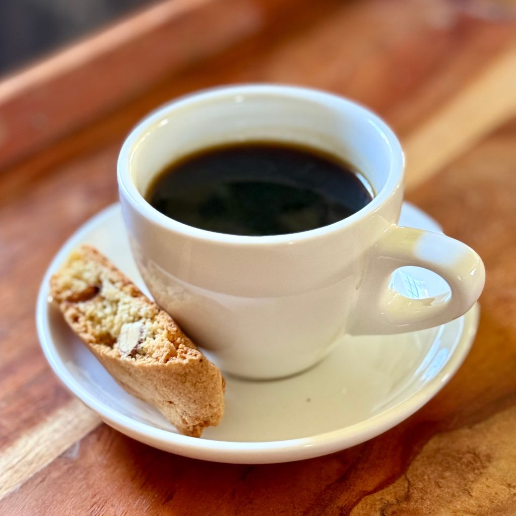 A rustic plate of chocolate almond biscotti next to a cup of espresso and scattered almonds