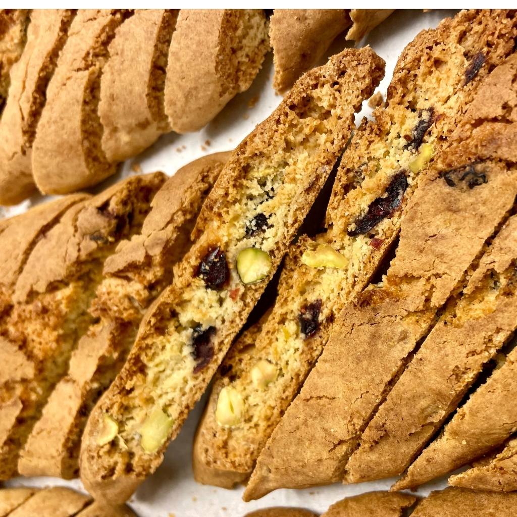 Fresh cranberry pistachio biscotti straight from the oven with full slices and two on their side showing bright red cranberries and green pistachios