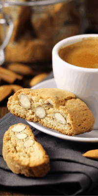 Two almond biscotti next to a cappuccino, one biscotti resting on the saucer
