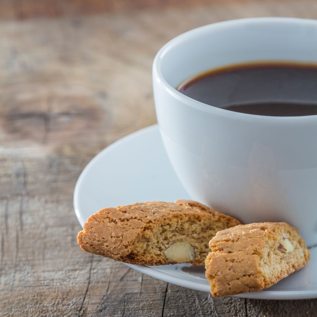 Cup of coffee on a saucer with two almond biscotti on a wooden table