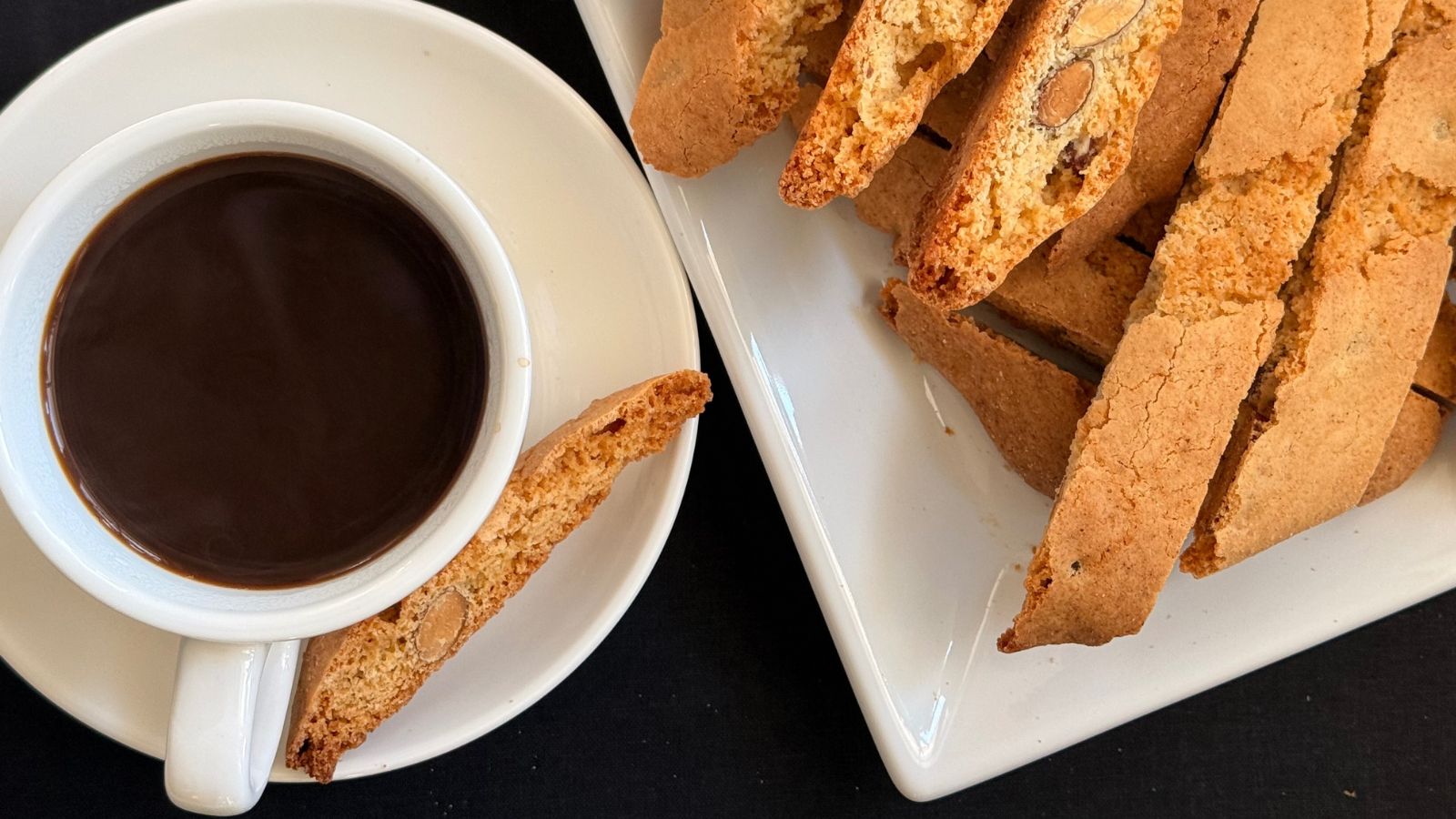 Almond biscotti served with black coffee on a white plate, showing crisp sliced biscotti in a classic Italian café-style setting