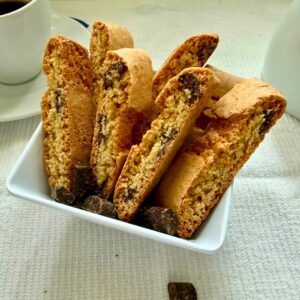 Chocolate chunk biscottini standing in a white dish with coffee cups in the background