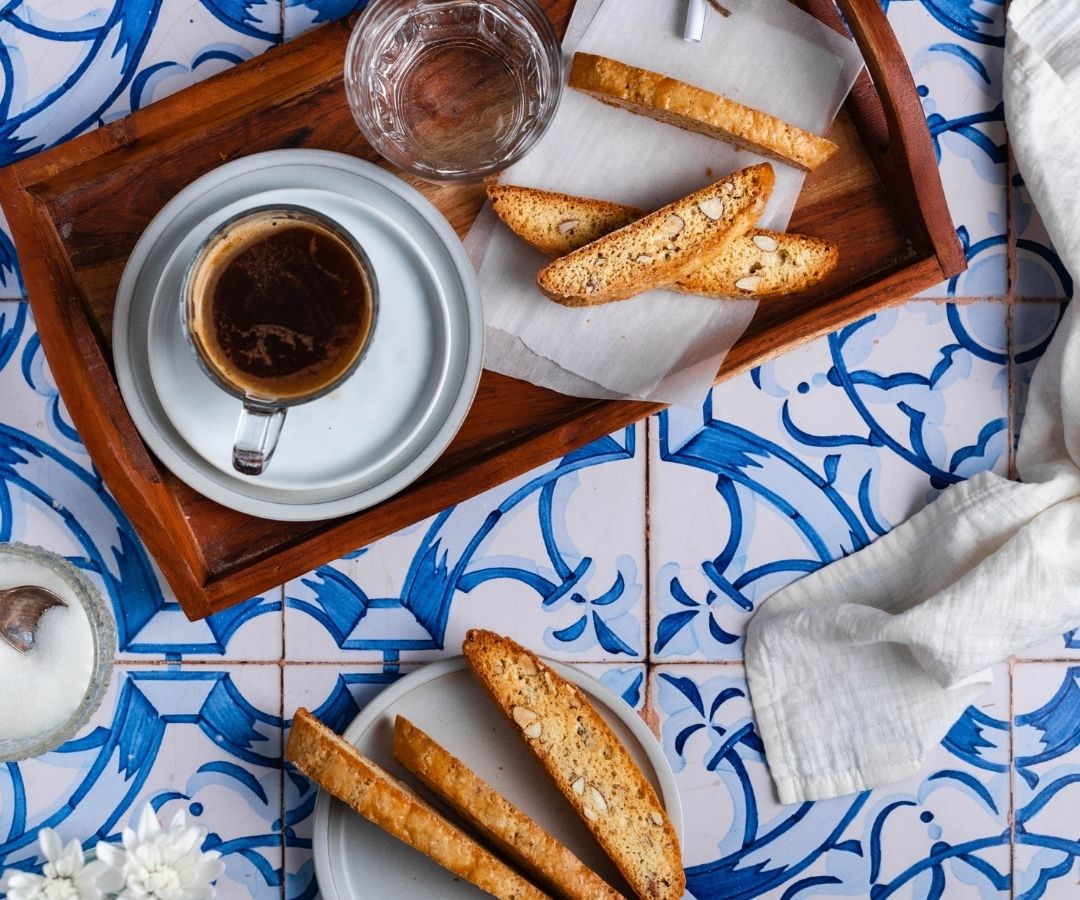 Classic almond biscotti served with espresso on a wooden tray over blue Italian tile