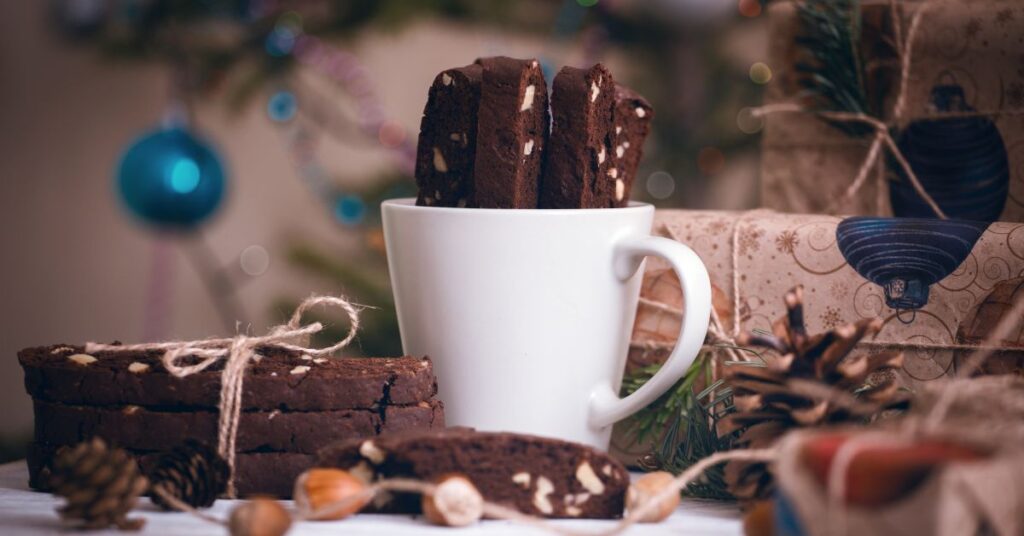Double Chocolate Biscotti in a white cup with a festive holiday background of warm lights and greenery.