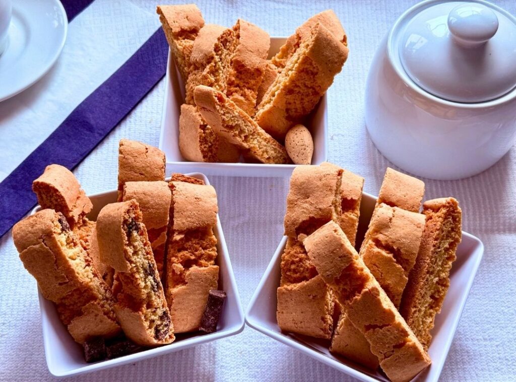 Three dishes of biscottini showing almond, amaretto, and chocolate flavors arranged together with coffee