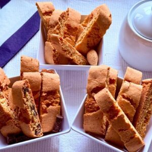 Three dishes of biscottini showing almond, amaretto, and chocolate flavors arranged together with coffee