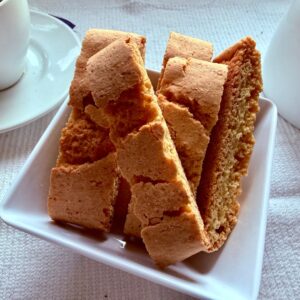 Lemon biscottini standing in a white dish with coffee cups in the background