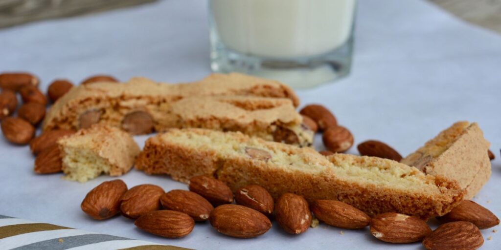 Classic almond biscotti slices baked twice for a crisp snap, surrounded by whole almonds with a glass of milk in the background