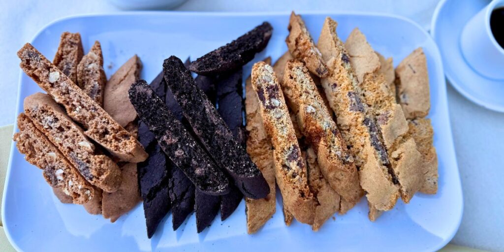 Assorted biscotti cookies on a white platter with a cup of coffee in the background.
