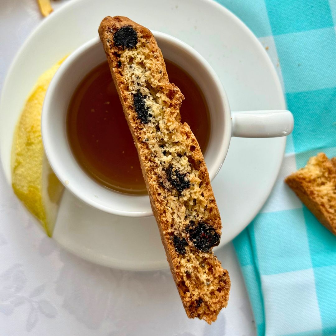 Blueberry lemon biscotti resting on a cup of tea with a lemon wedge