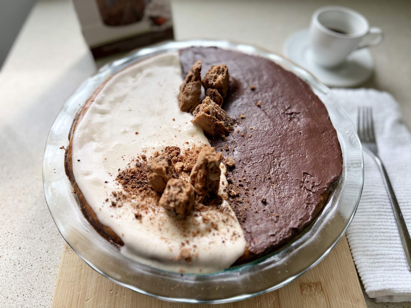 Whole biscotti cheesecake in a pie dish with black-and-white chocolate and vanilla topping and Chocolate Hazelnut Espresso biscotti shards
