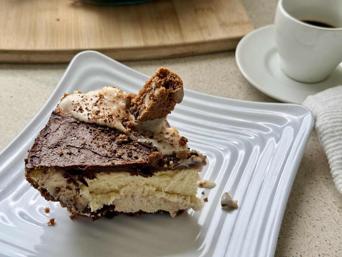Slice of biscotti cheesecake on a white plate served with a cup of espresso and a Chocolate Hazelnut Espresso biscotti shard